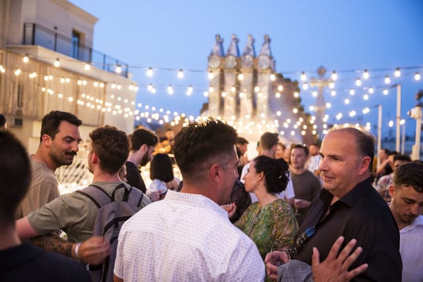 Guests talking on the roof terrace at dusk under string lights with mosaic chimneys behind