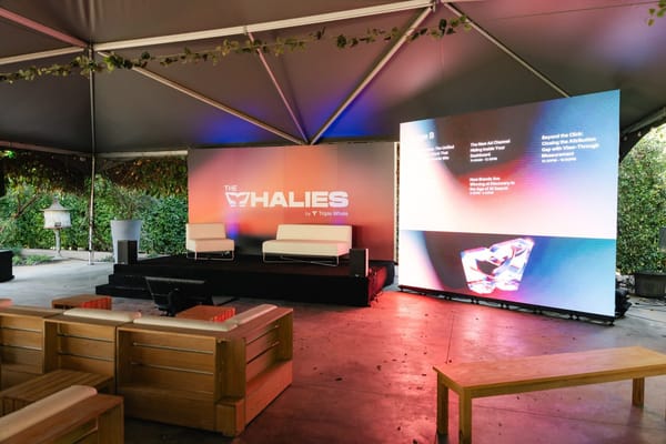 Wooden benches facing a stage and a large screen inside the tent