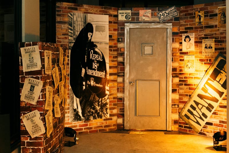 Brick speakeasy front with a plain door, WANTED posters and a print reading Repeal the 18th Amendment