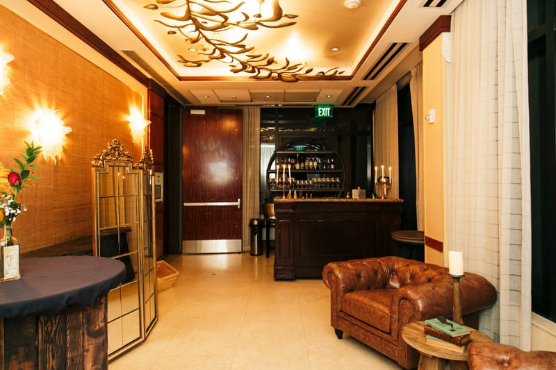 Lounge corner with a leather chesterfield chair, a round table, a gold wire screen and a bar behind