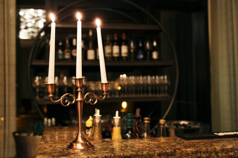 Brass candelabra with three lit candles on a bar in front of shelves of bottles and glasses