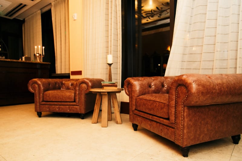 Two brown leather chesterfield armchairs around a small wooden table in a curtained lounge