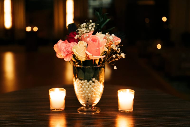 Pink and cream roses in a glass vase filled with pearls between two tea lights