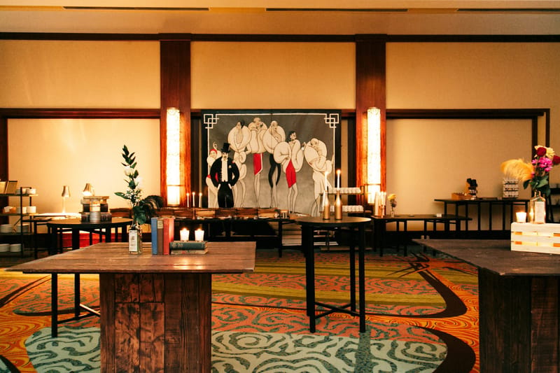 Wooden tables before a painted backdrop of women in white fur wraps and a man in a top hat