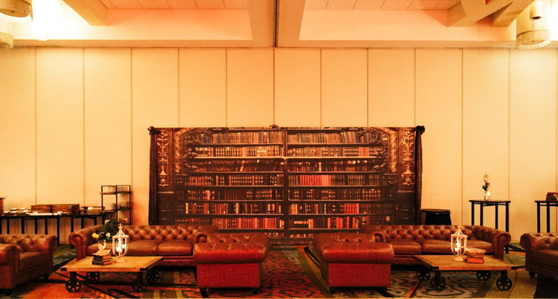 Leather chesterfield sofas and coffee tables in front of a backdrop printed with bookshelves