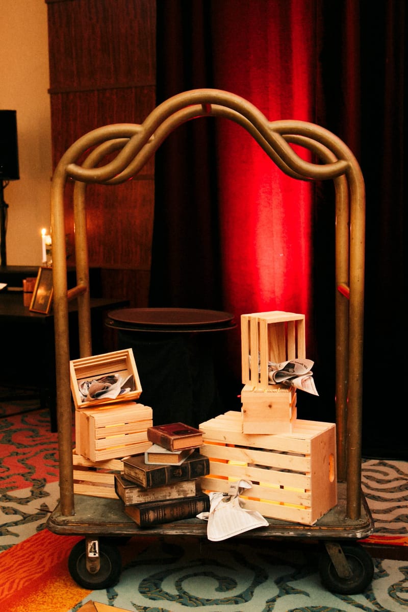 Brass luggage cart holding wooden crates, old books and small photographs