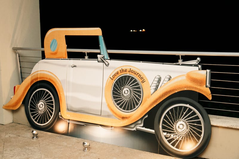 Flat cutout of a white and orange vintage car reading Love the Journey, along a railing at night