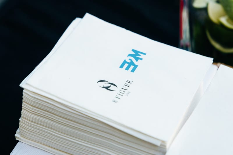 Stack of white napkins printed with the 8 Figure Live and E2M logos