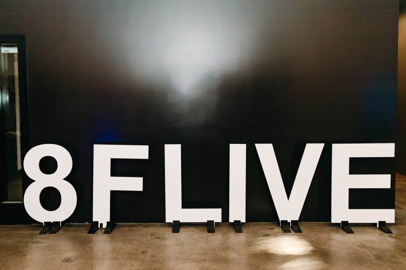 White 8FLIVE letters standing against a black wall under a spotlight