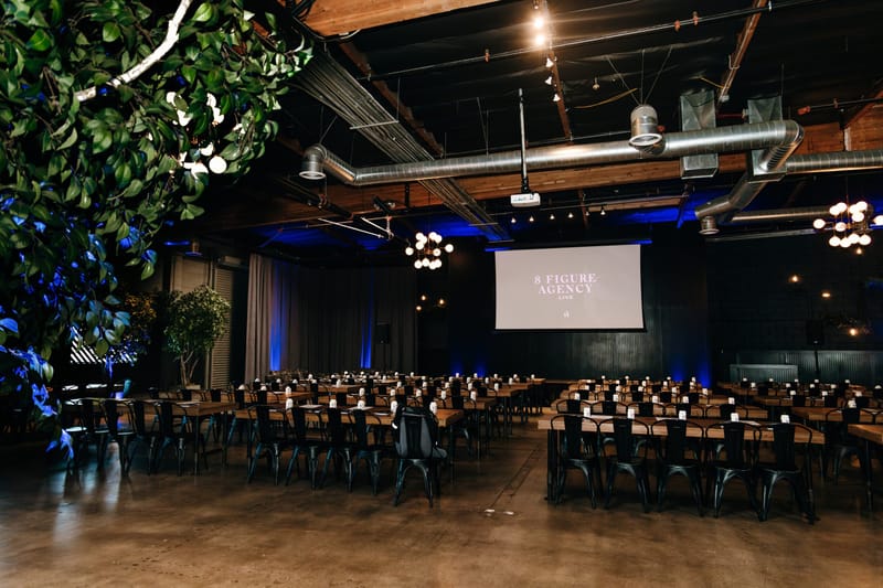 Long view of the hall with rows of tables under hanging greenery and globe lights