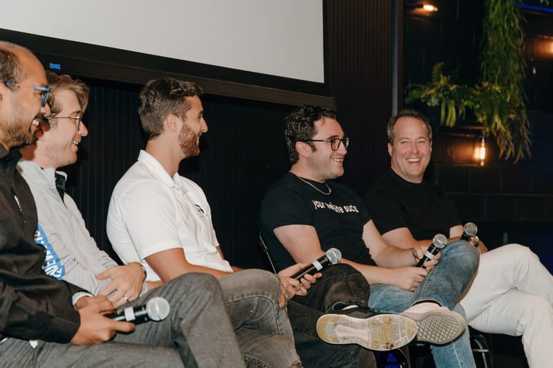 Panelists laughing together on stage, each holding a microphone under hanging plants