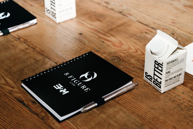 Black 8 Figure Live notebook and pen beside a boxed water carton on a wooden table