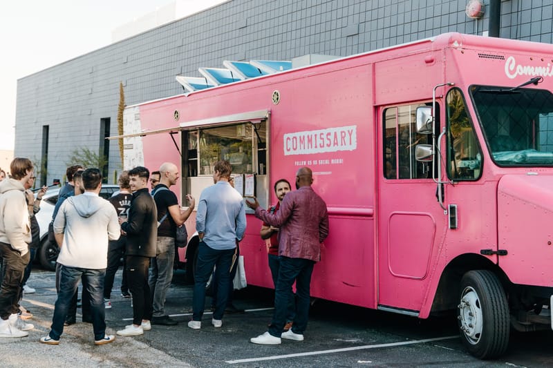 Attendees lining up at a pink Commissary food truck in a parking lot