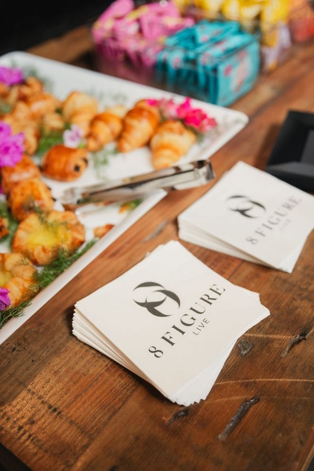 Pastries with pink flowers beside a stack of 8 Figure Live napkins