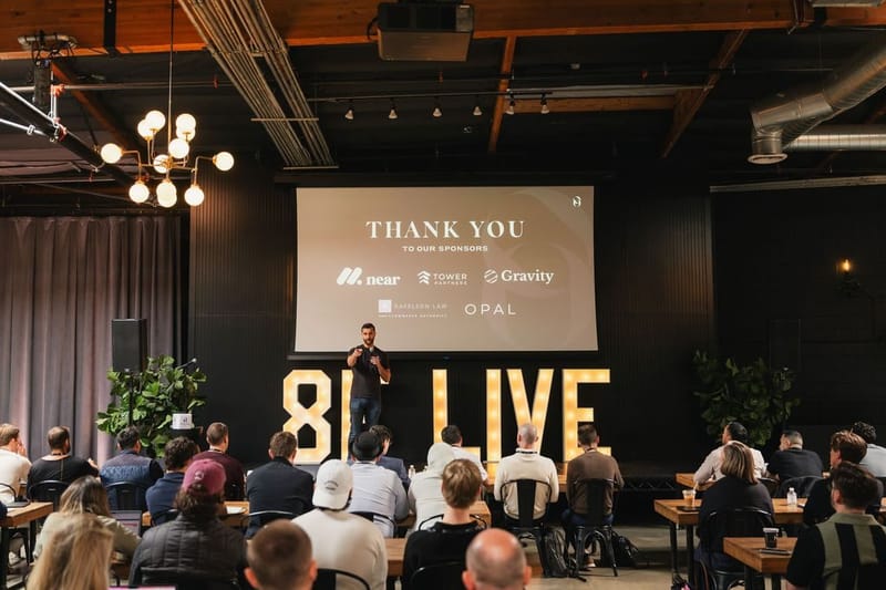 A speaker on stage in front of the 8F LIVE letters addressing a seated audience