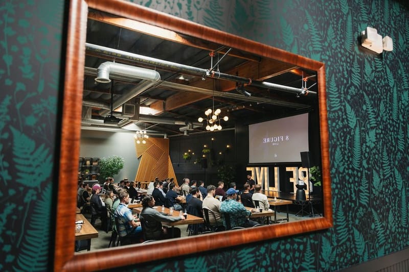 The full conference room reflected in a wood-framed mirror on a dark green wall