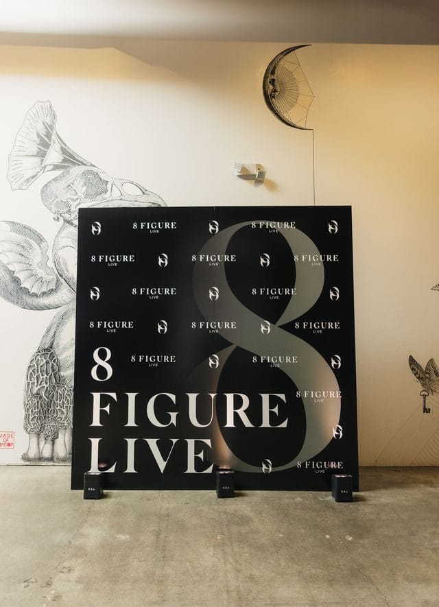 Black 8 Figure Live logo backdrop standing in a hallway with botanical wallpaper