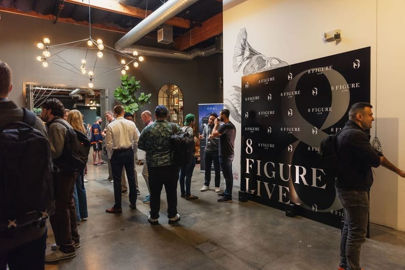 Attendees networking in a hallway beside a black 8 Figure Live logo backdrop