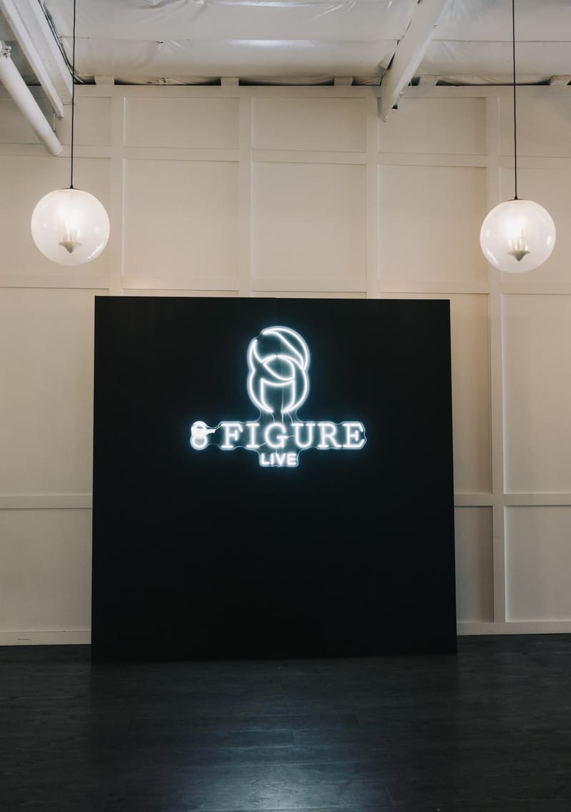 Illuminated 8 Figure Live logo on a black backdrop between two globe pendant lights