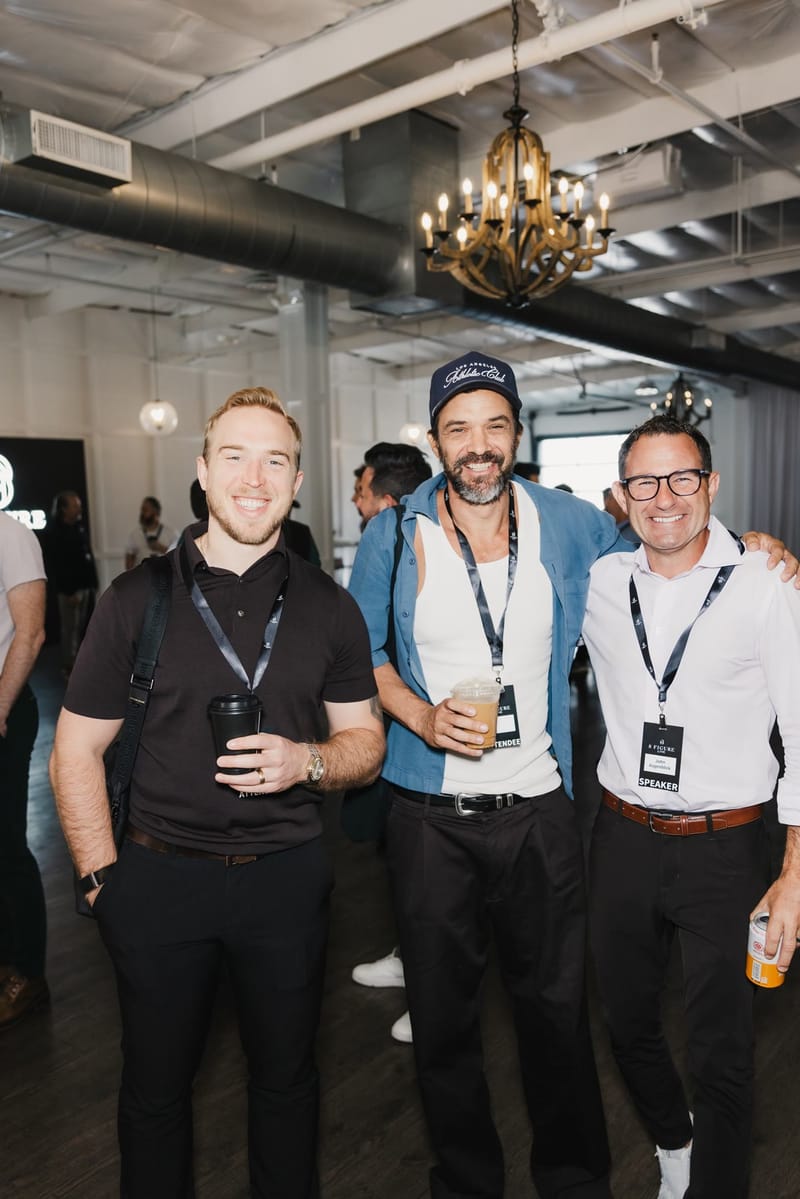 Three attendees wearing 8 Figure Live lanyards smiling together under a chandelier