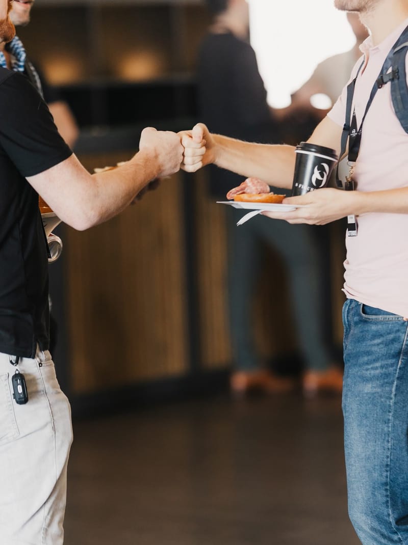 Two attendees bumping fists while holding a coffee and a plate