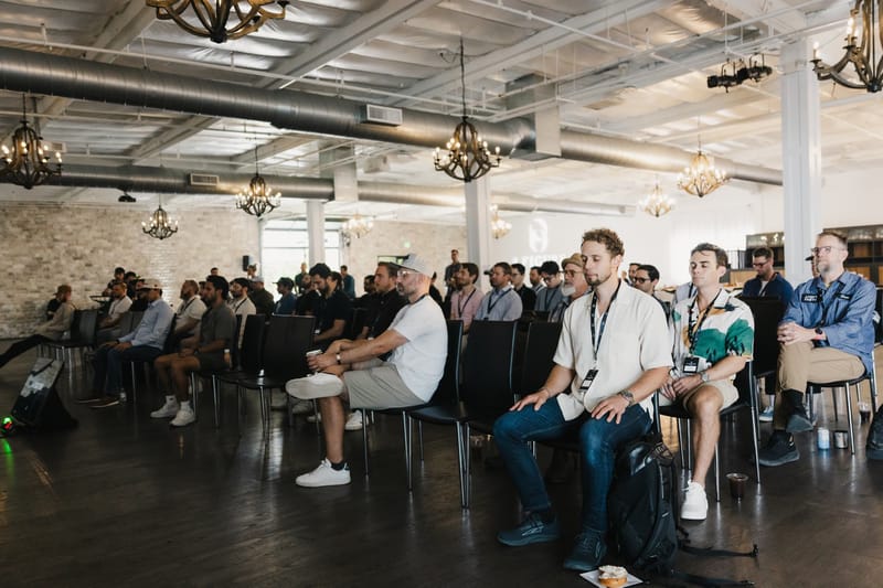 Attendees seated in rows under chandeliers and exposed ducts at 8 Figure Live OC
