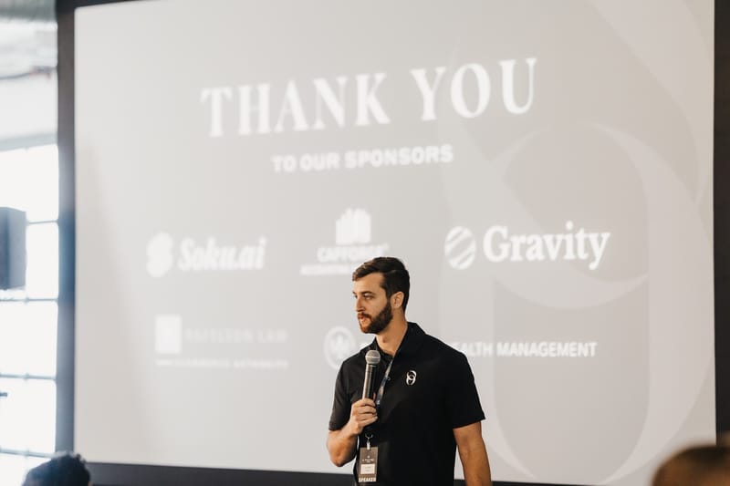 Host with a microphone in front of a thank you to our sponsors slide
