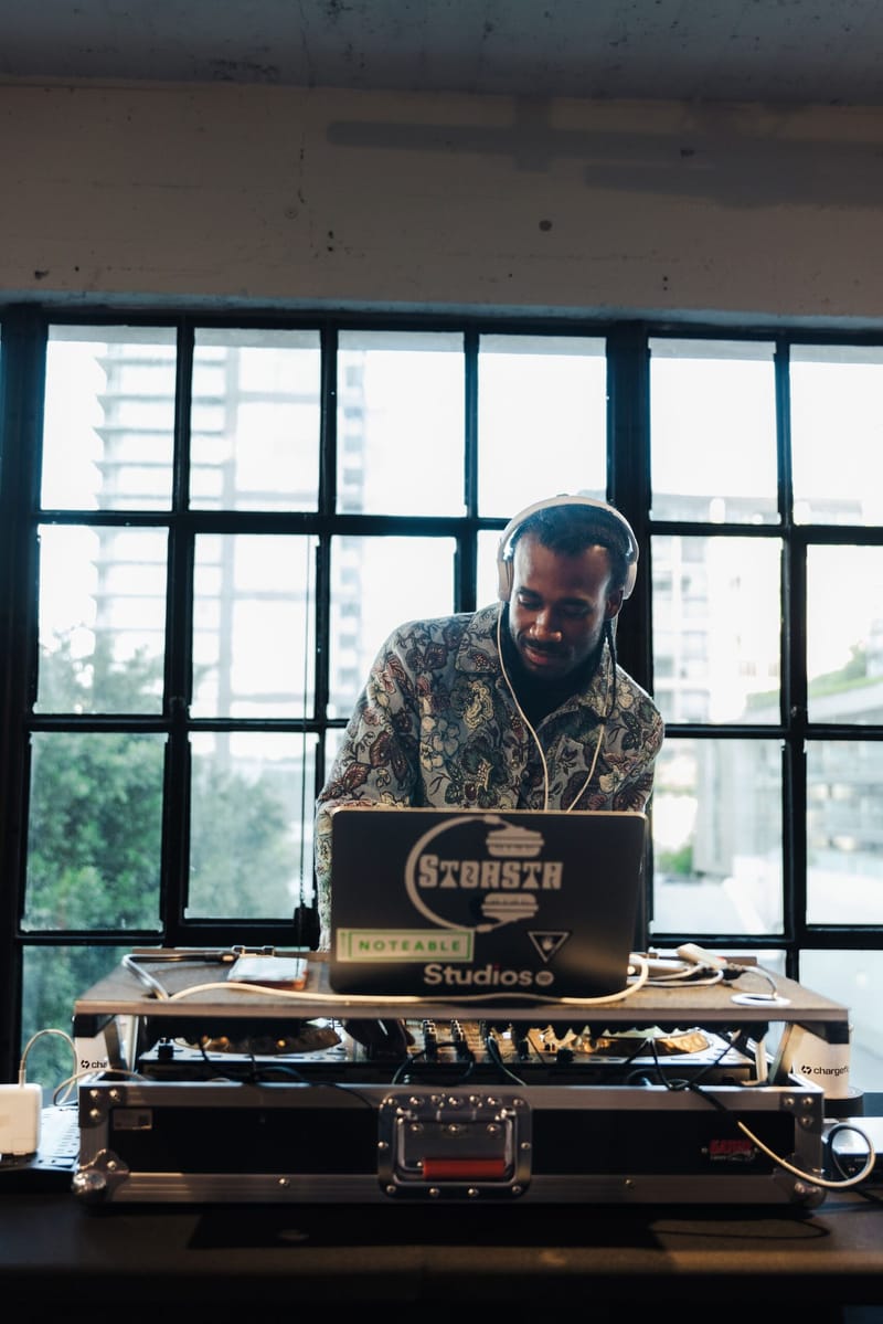 A DJ in headphones playing at decks with a laptop