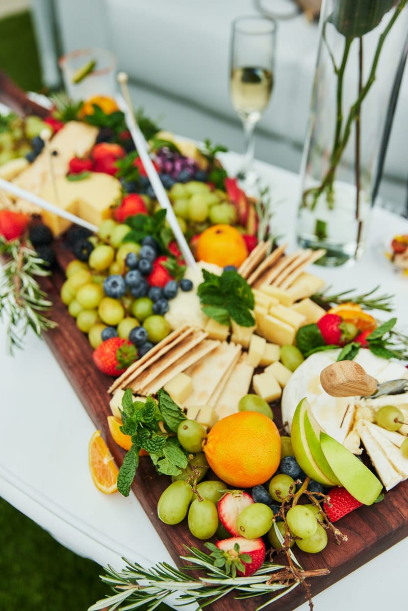 Wooden board of cheese, crackers, grapes, berries and oranges with rosemary and a glass of champagne