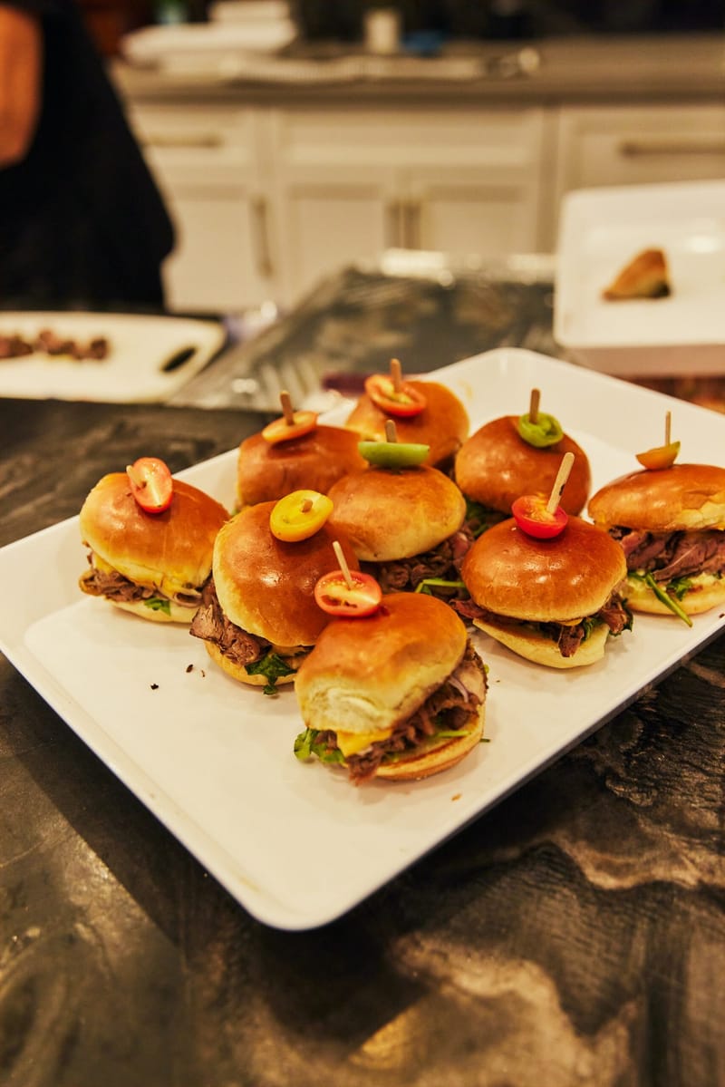 Sliders held with wooden picks and small colorful garnishes on a white platter