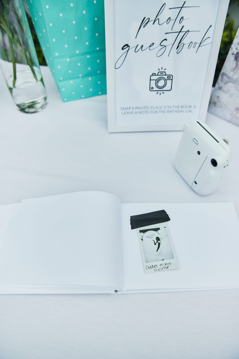 Photo guestbook sign asking guests to leave a note for the birthday girl, with an instant camera and open book