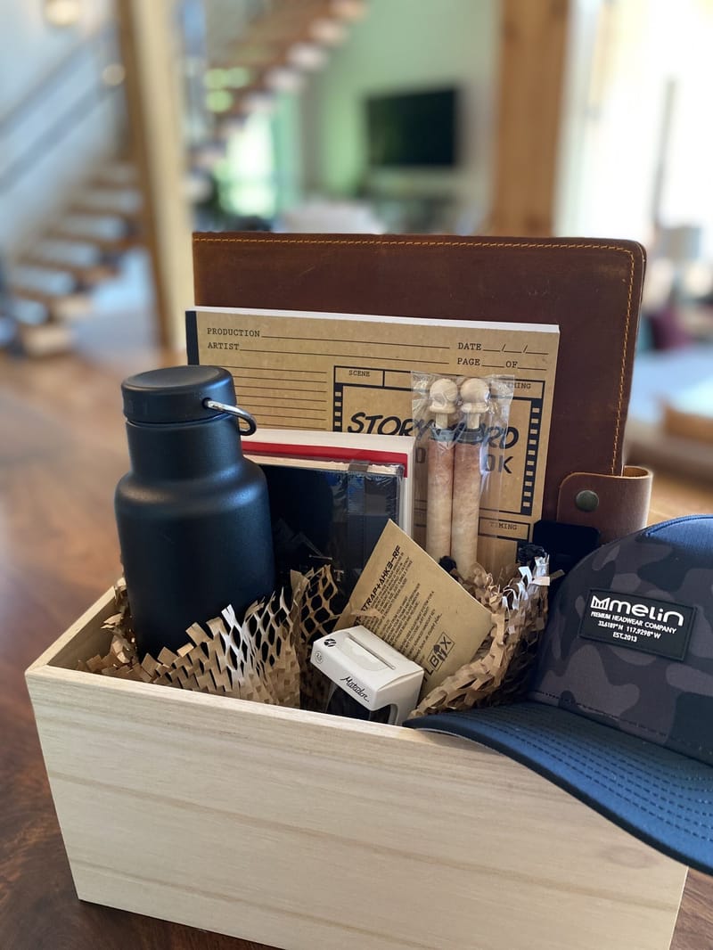 Wooden welcome box holding a leather portfolio, Storyboard notebook, black bottle and a camo Melin cap