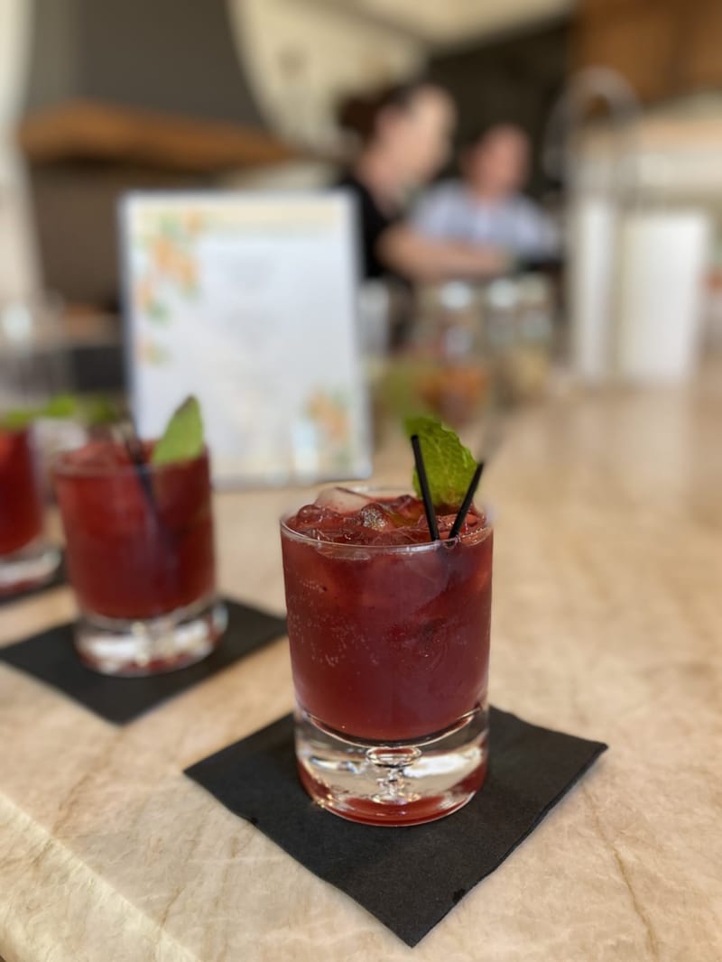 Red cocktail with mint and black straws on a black napkin, a menu card blurred behind
