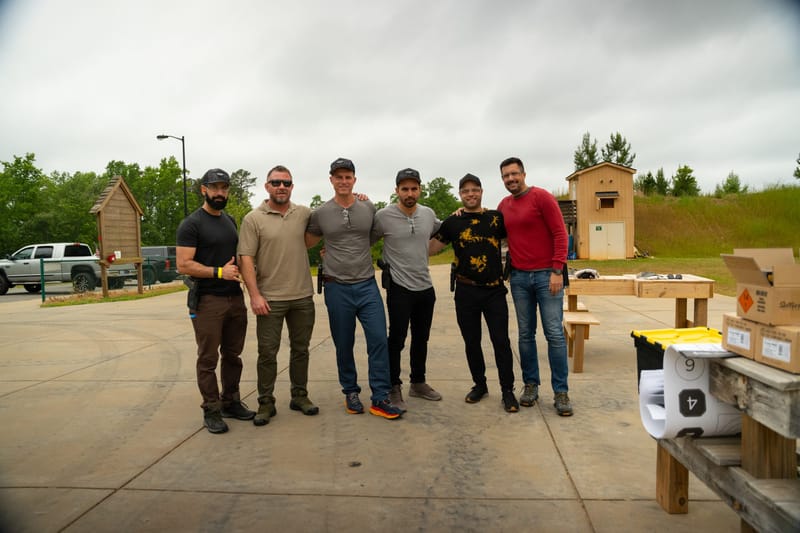 Six guests posing outdoors beside boxes and rolled paper targets
