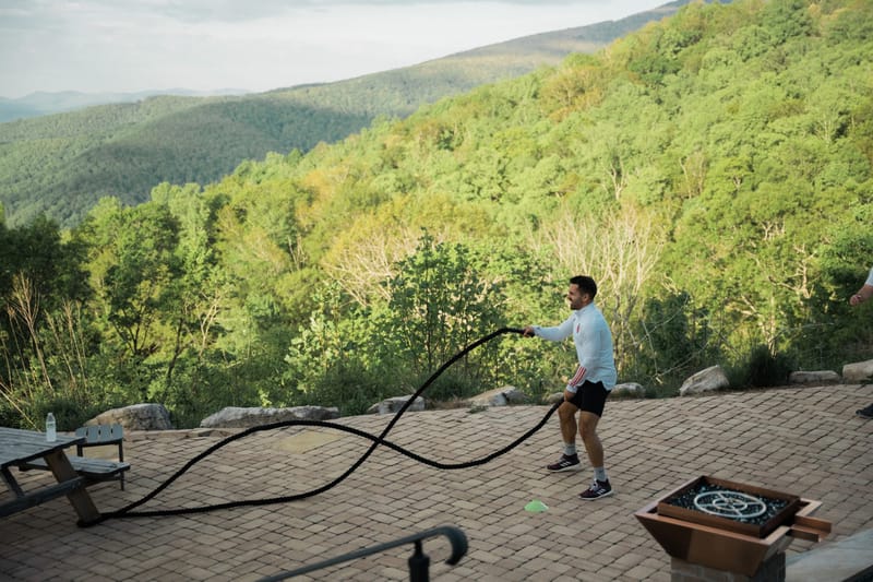 A guest working out with battle ropes on a stone patio above a forested valley