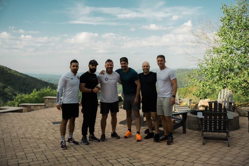 Six guests posing together on a brick patio with mountains and a cloudy sky behind