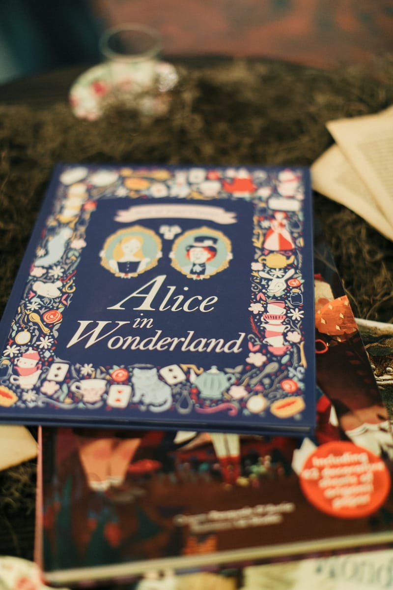 Navy illustrated copy of Alice in Wonderland resting on a bed of moss