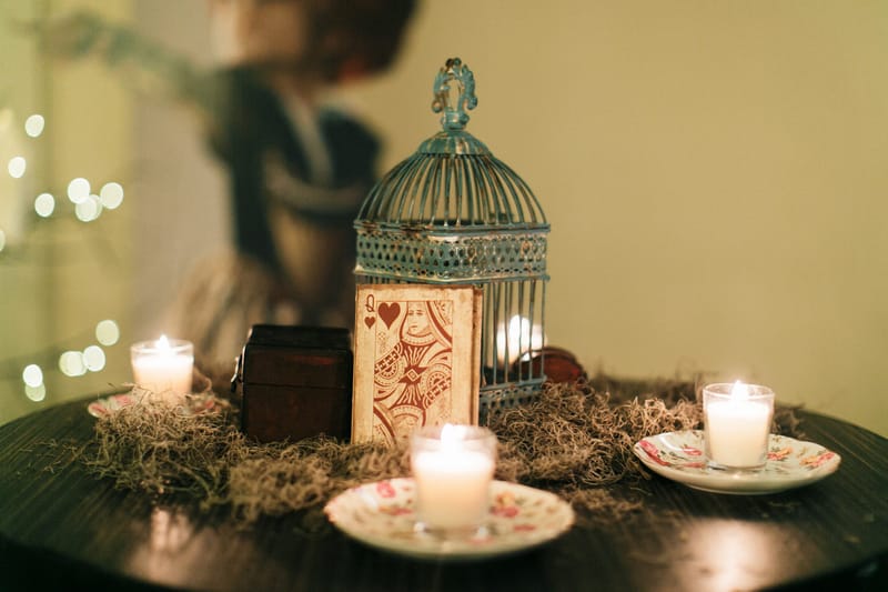 Birdcage lantern, a heart playing card, a small chest and votive candles on floral saucers