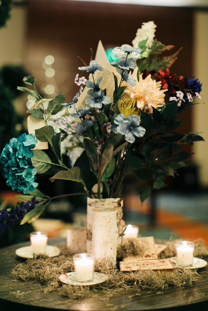 Blue and white flowers in a birch-wrapped vase with votive candles on moss
