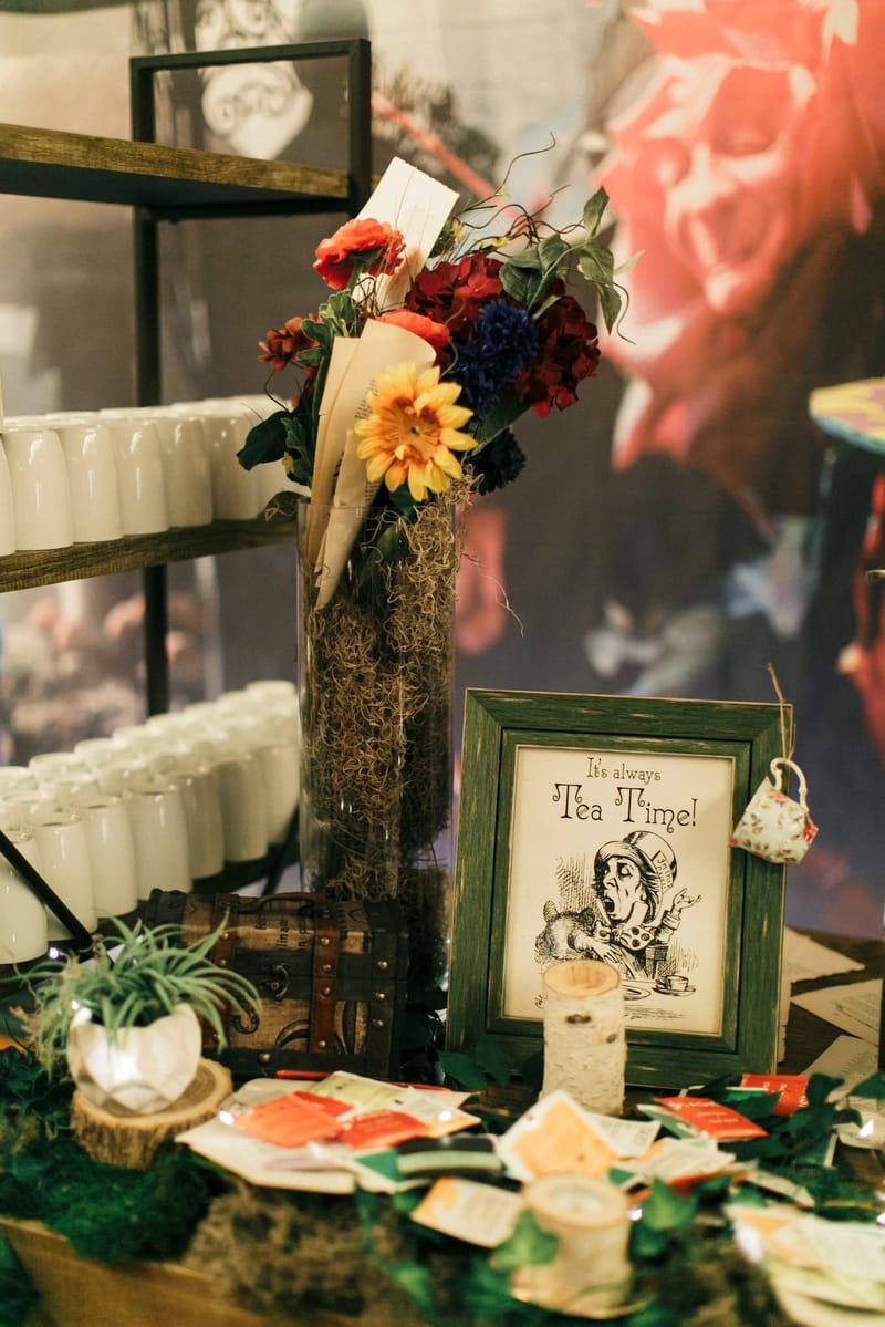 Framed Mad Hatter print reading It's always Tea Time! with a tiny teacup hanging from the frame