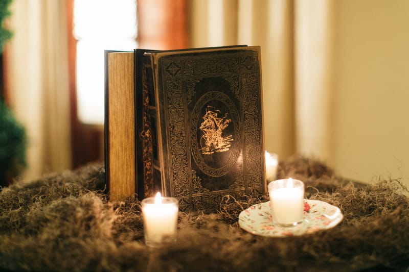 Ornate old book with an embossed cover beside votive candles on a bed of moss