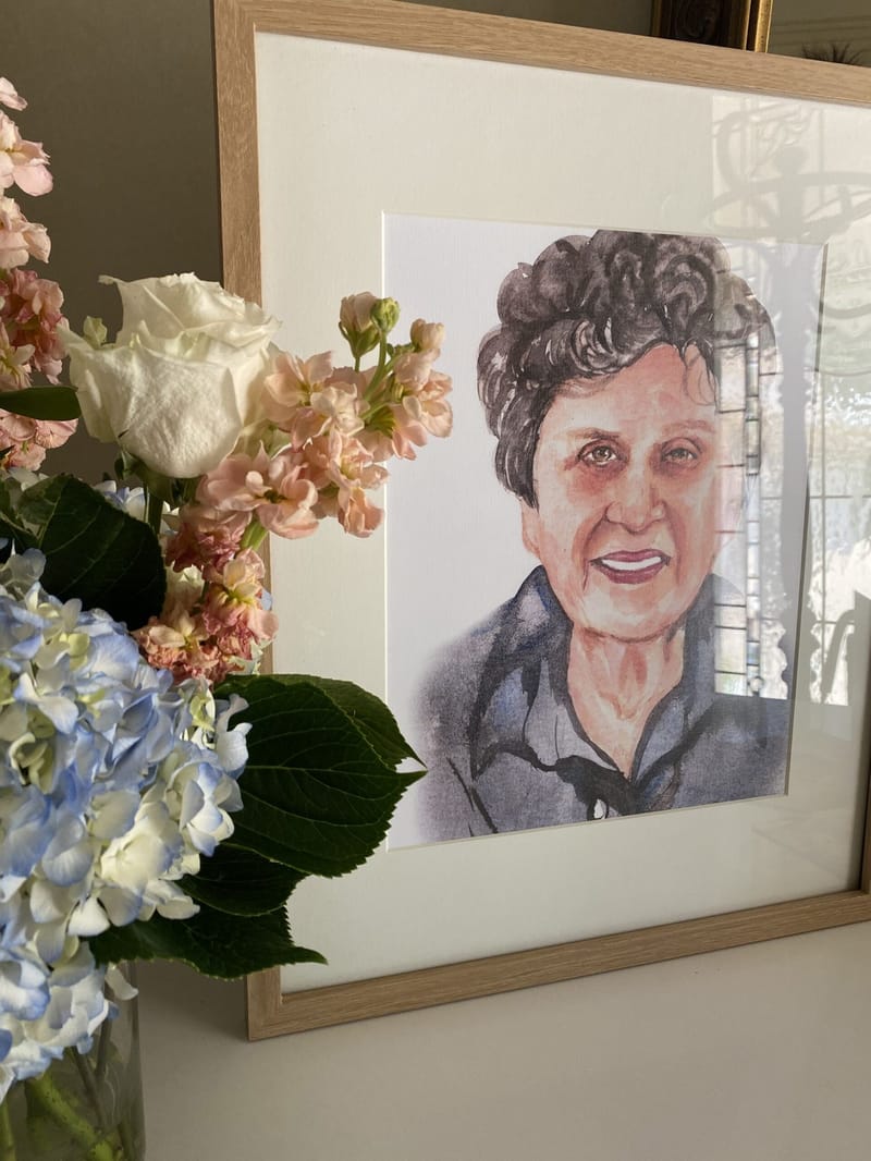 Framed watercolor portrait of a smiling woman with short dark curls beside hydrangeas, roses and pink stock