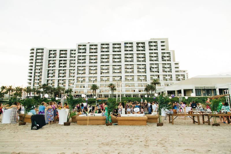 Guests gathered at lounge tables on the beach in front of a tall white hotel building