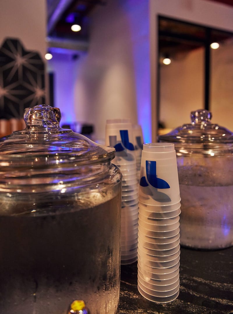 Glass drink dispensers beside stacks of cups printed with the Triple Whale logo