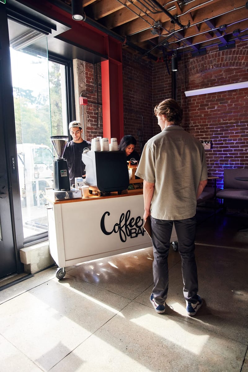 Guest waiting at a Coffee Bar cart while a barista works by an open doorway