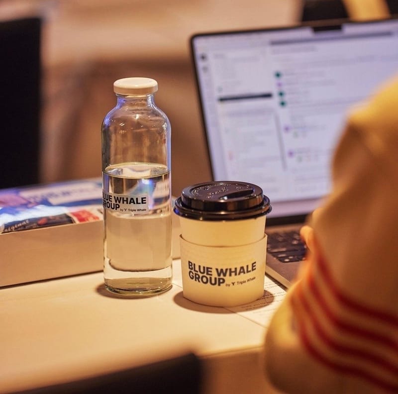 Blue Whale Group water bottle and coffee cup beside an open laptop