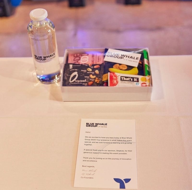 Welcome letter from Blue Whale Group, a labeled water bottle and a box of snacks on a white table
