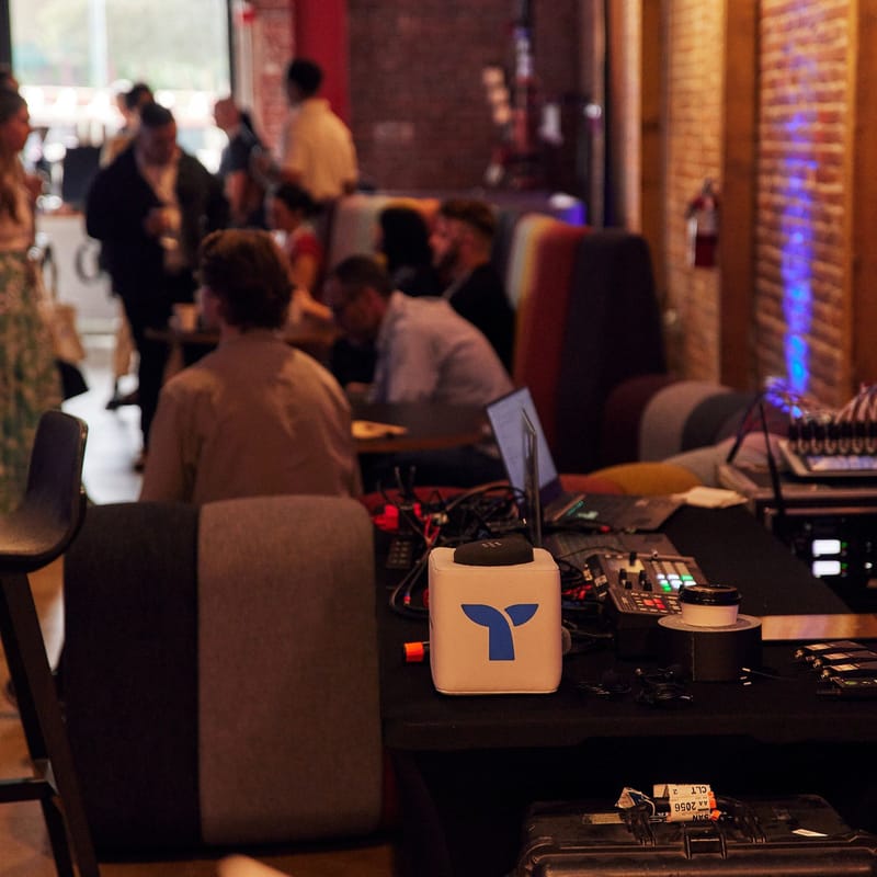 Audio desk with a small cube printed with the Triple Whale logo as attendees talk nearby