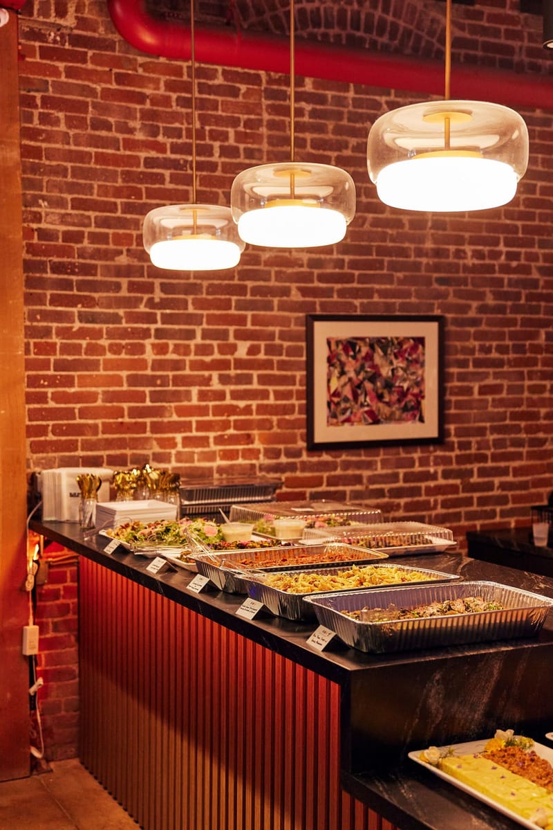Buffet counter of catering trays under glass pendant lights against a brick wall