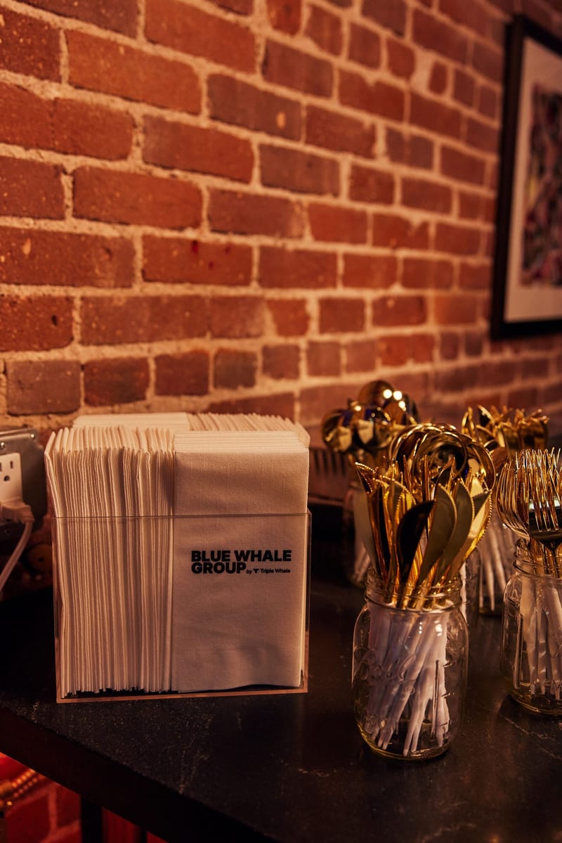 Blue Whale Group napkins and a jar of gold cutlery on a dark counter